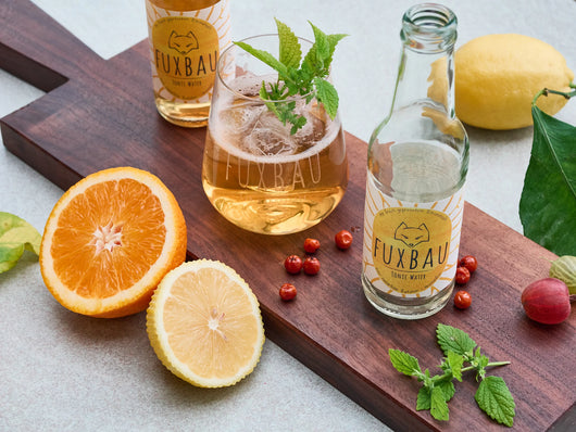 Fuxbau Tonic Water serviert auf einem Holzbrett mit MInze, Vogelbeeren, Orangen und Zitronen